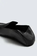 Mocasín de cuero negro, de estilo clásico y minimalista, con suela fina y horma cuadrada.