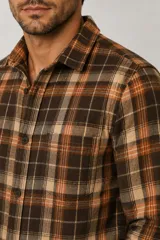 Sobrecamisa de franela a cuadros en tonos marrón, tostado, naranja y blanco, de manga larga con cierre frontal de botones y un bolsillo en el pecho.