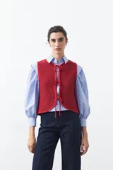 Chaleco de punto con efecto jaspeado en color azul, con diseño sin mangas, escote redondeado y cierre frontal mediante lazos ajustables.