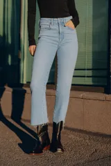 Jeans de tiro alto color marrón oscuro con acabado lavado, corte recto/flare y bajo cropped sin costuras. Presenta cinco bolsillos y cierre frontal con cremallera y botón metálico.