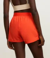 Bermuda deportiva color naranja, confeccionada en tejido técnico transpirable con tecnología Dry. Presenta cintura elástica, bolsillos laterales y cordones laterales ajustables que permiten fruncir el largo de la prenda.