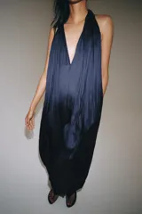 Mono largo satinado de color azul marino, con cuello halter, escote en V profundo y espalda descubierta. Presenta diseño plisado y bajo abullonado con terminación en puño.