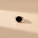 Anillo tipo sello de plata 925 con centro circular de resina negra. Diseño minimalista con banda de ancho variable.