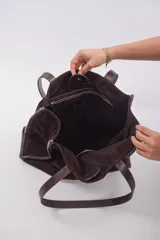 Bolso tipo shopper de gran tamaño, confeccionado en cuero gamuzado color marrón. Presenta estructura rectangular con bordes reforzados en cuero liso oscuro, doble asa de hombro y cierre mediante botón magnético.