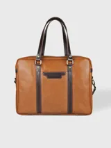 Maletín morral de cuero color marrón con detalles en marrón oscuro, hecho en Uruguay. Tiene doble asa de mano y correa bandolera desmontable. Cuenta con un compartimento principal con cierre y un bolsillo frontal con el logo de la marca.