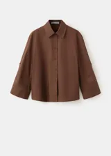 Camisa de algodón color marrón, de diseño recto, con cuello camisero, manga larga con puños abotonados y cierre delantero con botones.