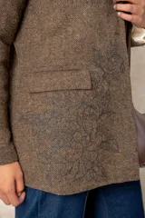 Blazer de corte sastre con diseño de espiga en tonos grises. Presenta un bordado floral lineal en el lateral, solapas clásicas, cierre frontal con un botón y bolsillos con solapa.