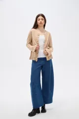 Saco de punto color gris, con cuello redondo, cierre frontal con botones y detalle de volados en la tapeta y el ruedo. Presenta mangas largas con puños acampanados.