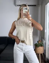 Blusa blanca sin mangas, de símil lino, con cuello alto y detalle de encaje calado y volados en el escote.