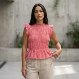 Musculosa sin mangas con estampado de cuadros vichy en tonos rojo y blanco, cuello redondo y diseño fruncido en el cuerpo. Cuenta con volados pequeños en los hombros y tiras ajustables con lazos en los laterales de la cintura.