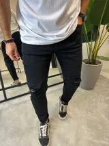 Jean de corte skinny color negro, con diseño de roturas en la rodilla y acabado desgastado. Presenta cierre frontal con botón y bolsillos laterales.