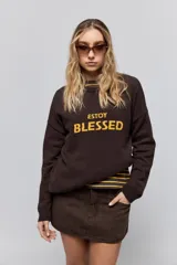 Sweater de punto marrón de tejido liviano y calce relajado, con hombros caídos, cuello redondo y puños y cintura en rib. Cuenta con una estampa tejida en el frente con la frase "Estoy Blessed" en color amarillo.