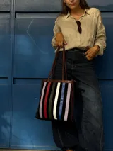 Cartera tipo tote de cuero con diseño de franjas verticales multicolores en tonos tierra, rojo y azul. Cuenta con correas trenzadas de cuero y cierre superior.