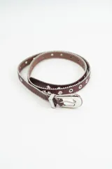 Cinturón color bordeaux con detalle de tachas metálicas en los bordes y ojales metálicos a lo largo de toda la tira. Incluye hebilla metálica plateada con diseño labrado.