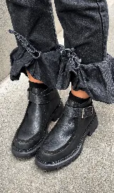 Bota corta tipo borcego de cuero negro, con suela track liviana y detalle de tira con hebilla metálica en el tobillo.