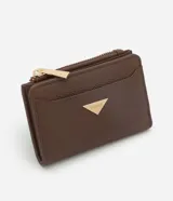 Billetera compacta Satinato de cuero sintético color marrón, con diseño tipo sobre. Cuenta con cierre metálico, botón a presión, monedero integrado y detalle de chapa triangular dorada con el logo de la marca en el frente.