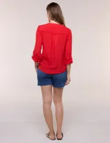 Blusa de calce relajado color salmón, confeccionada en tela liviana con textura sutil. Presenta escote en V con abotonadura frontal, bolsillo parche en el pecho, mangas largas regulables con presilla y ruedo con opción de anudar en el frente.
