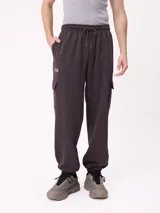 Babucha de estilo cargo en color gris oscuro, confeccionada en tejido de algodón y poliéster. Presenta cintura elástica con cordón de ajuste, bolsillos laterales tipo cargo con solapa y puños elásticos en los tobillos. Incluye un pequeño logo bordado en la parte superior de uno de los bolsillos.