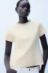 Jersey de punto color amarillo claro, con cuello redondo adornado con aplicación de joyas a contraste, manga corta y cierre en la espalda con abertura y botón.