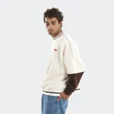 Buzo crewneck de corte boxy y mangas murciélago, con diseño bicolor en azul y blanco. Presenta letras bordadas en el frente y detalles de líneas horizontales en cuello y ruedo.