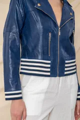 Chaqueta azul de cuero ecológico con cierre frontal asimétrico y cuello con solapas. Tiene puños elásticos a rayas blancas y azules, cierres metálicos plateados y un bolsillo en la manga.