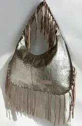 Cartera de hombro color dorado con textura símil cocodrilo y flecos colgantes en los bordes y las asas, de la marca Carolina de Cupto.