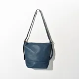 Bandolera azul de cuero sintético con textura granulada. Tiene correa larga regulable, cierre superior y bolsillo interno.