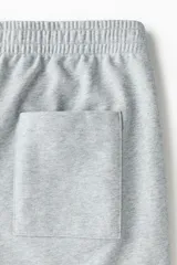 Pantalón jogger de punto de algodón gris melange, de corte relajado y perneras rectas con pliegue frontal cosido. Presenta cintura elástica con cordón ajustable, bolsillos laterales y falsas braguetas decorativas.