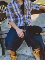 Camisa de manga corta con corte híbrido boxy fit/oversize, confeccionada en algodón. Disponible en tres diseños: a cuadros marrones, a rayas blancas y negras, y a rayas burdeos y blancas. Presenta bordados de diseño propio de la marca.