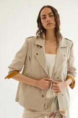 Chaqueta corta de inspiración motoquera color beige, confeccionada en lino fantasía, sin forro, con cierres decorativos, broches de presión y bolsillos delanteros funcionales. Presenta detalle bajo el cuello y en vueltas de mangas en color mostaza y rayas.