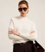 Blusa de punto acanalado color blanco, con cuello alto, mangas largas y puños ajustados. Confeccionada en viscosa, poliéster y poliamida.