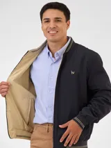 Campera bomber reversible azul marino y beige con cuello, puños y ruedo acanalados con rayas doradas. Tiene cierre frontal y logo bordado en el pecho.