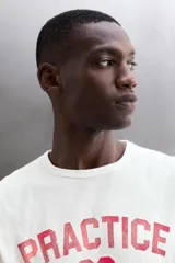 Camiseta de algodón gris melange con cuello redondo, mangas cortas y efecto lavado. Presenta un estampado de texto frontal en color oscuro con efecto desgastado.