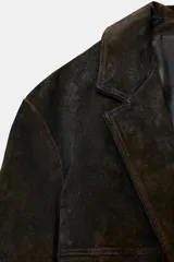 Blazer de piel de ante color marrón con efecto envejecido, solapas con muesca, cierre frontal de dos botones y bolsillos con solapa en el delantero. Cuenta con forro interior y costuras marcadas.