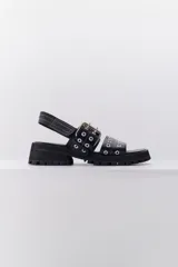 Sandalia de cuero negra con suela track, dos tiras frontales con ojalillos metálicos y hebillas grandes, y tira trasera con cierre de hebilla.