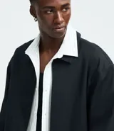 Campera masculina de corte boxy en color beige, con cuello inglés, cierre frontal de cremallera, mangas largas con puños elásticos y ruedo con elástico. Presenta bolsillos laterales y detalles de recortes en el diseño.