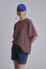 Remera oversize a rayas horizontales en tonos bordó y blanco, con cuello redondo verde oscuro y un pequeño parche bordado en forma de corazón en el pecho.