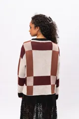 Buzo de tejido de punto con diseño geométrico de cuadros en tonos marrones, beige y bordó. Presenta cuello redondo, puños y borde inferior en color negro, con mangas largas y corte holgado.
