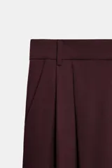 Pantalón de tiro medio con corte wide leg, presenta pliegues frontales, bolsillos laterales y trabilla con botón en la espalda. Cierre frontal con cremallera y botón.