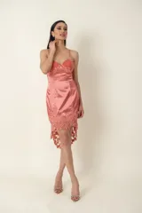Vestido corto de satén color salmón con diseño asimétrico. Presenta un bustier con detalles de encaje bordado en el escote y un ruedo con terminación en encaje floral. Posee breteles finos ajustables.
