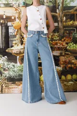 Jean de corte wide leg con diseño de tiro alto y piernas amplias. Presenta detalles de puntilla de crochet en los bolsillos delanteros y a lo largo de las costuras laterales, aportando un estilo romántico y distintivo.