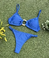 Bikini de dos piezas color azul vibrante. El corpiño es tipo top con un detalle de hebilla redonda dorada en el centro. La bombacha es colaless entera con frunces ajustables en los laterales.