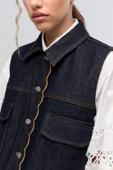 Chaleco de denim azul marino con cuello, bolsillos frontales y bordes festoneados.