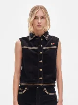 Chaleco de pana negro con cierre frontal de botones metálicos dorados. Presenta detalles de costuras en contraste en el cuello, cartera y canesú, e incluye un pequeño parche con forma de bandera en el pecho.