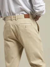 Pantalón de vestir color beige, de corte recto, con bolsillos laterales y traseros. Se ajusta a la cintura con cinturón de cuero marrón.