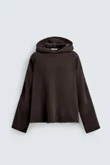 Sudadera de corte boxy fit en color marrón oscuro, con capucha, mangas largas y bandas laterales a contraste. Presenta un diseño de bajo con acabado irregular deshilachado.