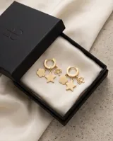 Caravanas tipo argolla pequeña en acero dorado, con tres dijes colgantes: una flor, una estrella y un diseño calado.