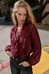 Blusa de escote en pico con volantes decorativos, manga larga con puños elásticos y cierre frontal con botones.