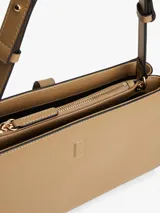 Cartera de hombro rectangular de color beige, confeccionada en poliuretano, con correa ajustable y cierre frontal mediante una tira con herraje metálico dorado con el logo de la marca.