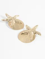 Par de aros dorados con forma de estrella de mar sobre una base circular con textura de concha.